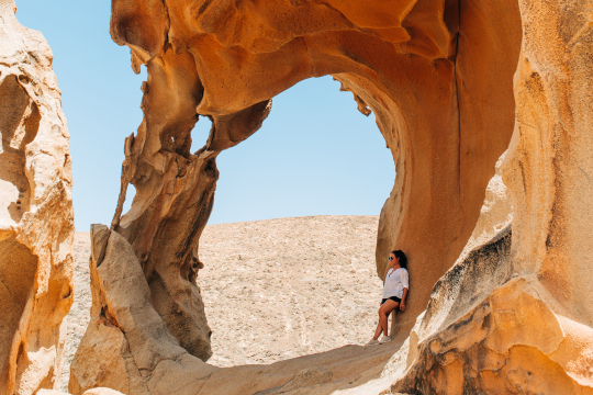 Eine Frau steht an einen braunen Felsen gewandt der wie ein Fenster geformt ist